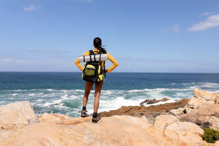 Fit afrcan american woman wearing backpack hiking on the coast. healthy lifestyle, exercising in nature.の写真素材