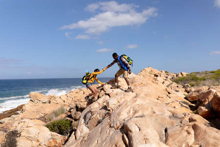 Fit afrcan american couple wearing backpacks hiking on the coast. healthy lifestyle, exercising in nature.の写真素材