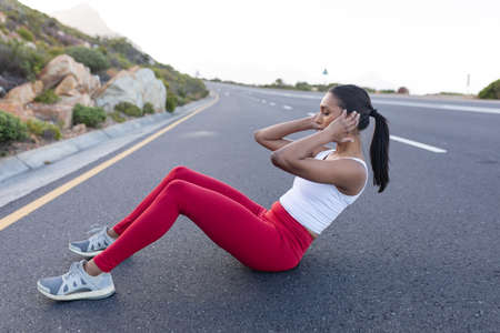Fit african american woman in sportswear doing crunches on a coastal road. healthy lifestyle,...
