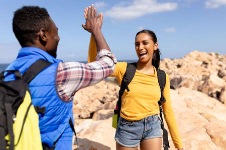 Fit afrcan american couple wearing backpacks high fiving hiking on the coast. healthy lifestyle, exercising in nature.の写真素材