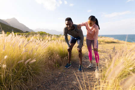 Fit african american couple in sportswear resting leaning on knees in tall grass. healthy lifestyle,...