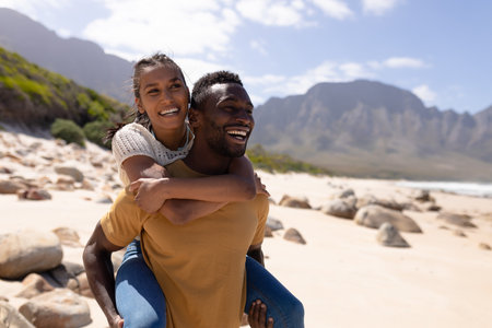 African american couple piggybacking on a beach by the sea. healthy lifestyle, leisure in nature.の写真素材