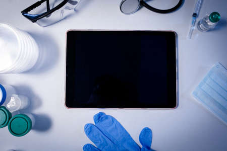 Desk in doctors surgery with tablet computer face mask gloves and stethoscope. telemedicine,...