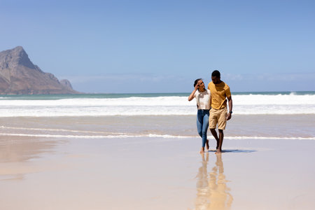 African american couple embracing walking on a beach by the sea. healthy lifestyle, leisure in nature.の写真素材