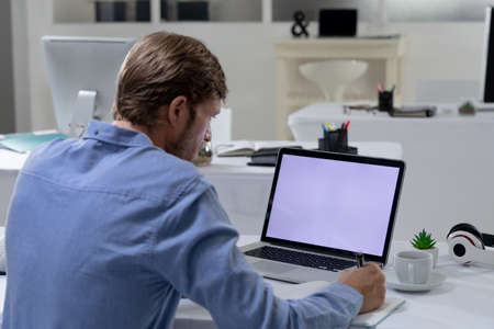 Caucasian businessman sitting at desk using laptop in an empty office. working online, social...