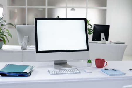 Desktop computer with illuminated screen and cup at workstation in abandoned office. working online,...