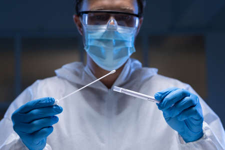 Caucasian male medical worker wearing protective clothing and face mask inspecting swab in lab....