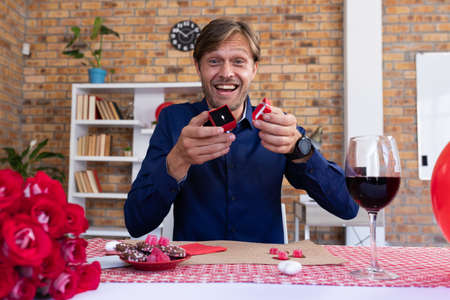 Caucasian man making video call opening a small gift box with ring and smiling. online communication...