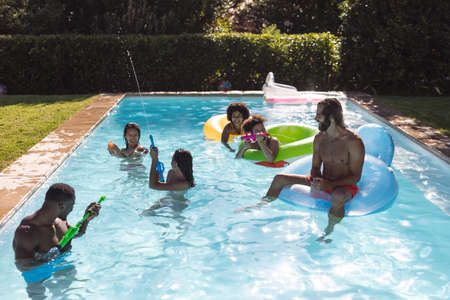 Diverse group of friends having fun playing on inflatables in swimming pool. Hanging out and...