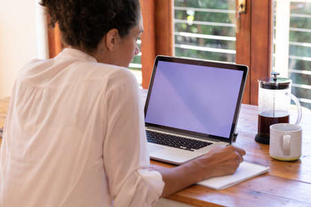 Caucasian woman using laptop working from home, making notes. Staying at home in self isolation during quarantine lockdown.の写真素材