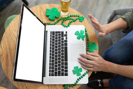 Caucasian woman waving making st patrick's day video call with laptop at a bar. fun during celebration of the irish patron saint's day.の写真素材
