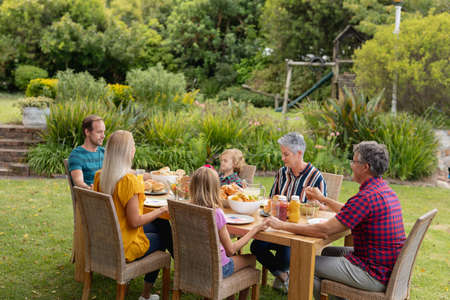 Caucasian three generation family holding hands saying grace before eating meal together in garden. three generation family celebrating independence day eating outdoors together.の写真素材