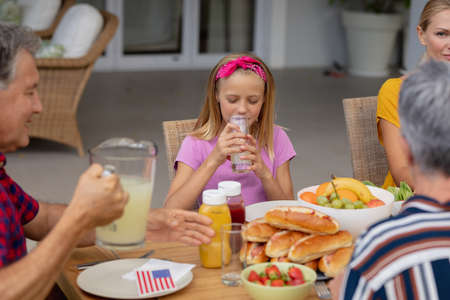 Smiling caucasian girl drinking lemonade sitting with family eating meal together in garden. three...