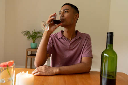 Mixed race man sitting at table and drinking wine. staying at home in isolation during quarantine lockdown.の写真素材