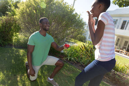 African american couple on sunny garden terrace a man proposing to her. staying at home in isolation during quarantine lockdown.の写真素材