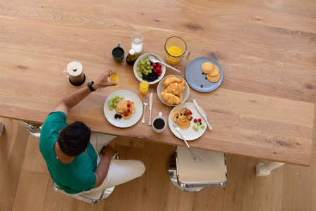 Mixed race man sitting at table and eating breakfast. staying at home in isolation during quarantine...