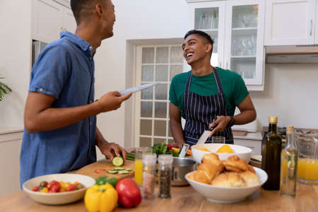 Diverse gay male couple spending time in kitchen cooking together and smiling. staying at home in isolation during quarantine lockdown.の写真素材