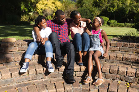 Smiling african american parents with daughter and son sitting embracing outdoors. staying at home in isolation during quarantine lockdown.の写真素材