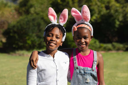 Portrait of happy african american brother and sister embracing wearing bunny ears outdoors. celebrating easter at home in isolation during quarantine lockdown.の写真素材