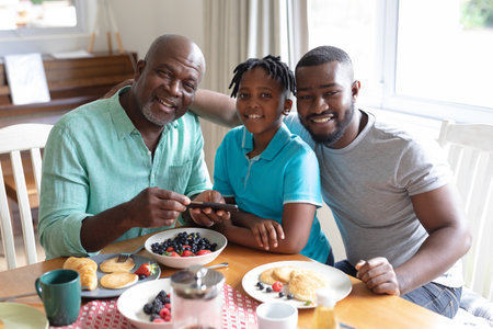 Happy african american father, grandfather and boy sitting at table and eating. three generation family spending quality time together.の写真素材