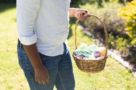 Midsection of african american boy holding basket while easter egg hunting. celebrating easter at...