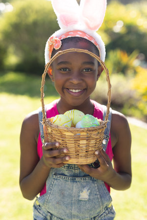 Portrait of african american girl holding basket while easter egg hunting. celebrating easter at home in isolation during quarantine lockdown.の写真素材