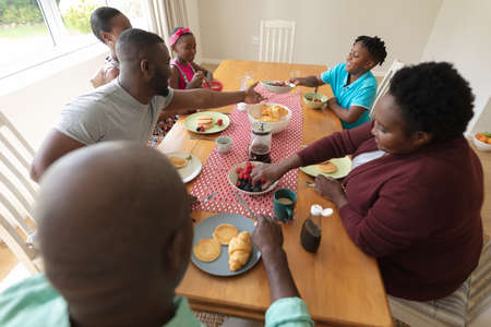 Happy african american parents, grandparents and grandchildren at table serving food and eating....