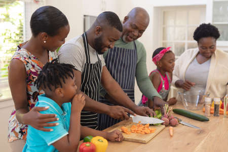 Happy african american parents cooking with son and daughter and grandparents in the kitchen. three generation family spending quality time together.の写真素材