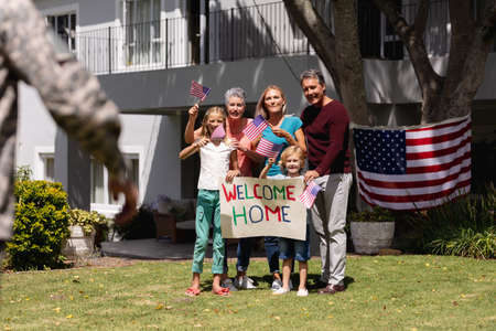 Caucasian soldier father and family meeting outside home with welcome sign and american flags....