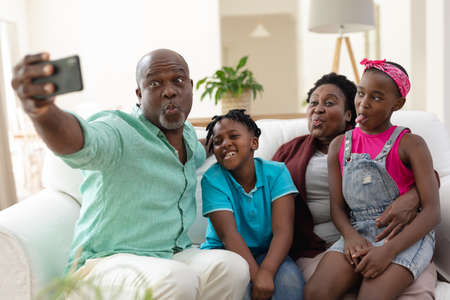 African american grandfather and grandmother on couch making faces with grandchildren taking selfie....