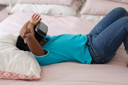African american boy wearing vr headset lying on his back on bed. staying at home in isolation...
