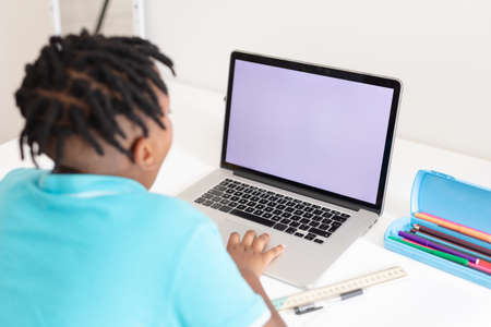 Rear view of african american boy at desk using laptop with copy space for online school lesson....