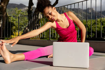 Mixed race woman exercising practicing yoga with a laptop on a terrace. staying at home in isolation...