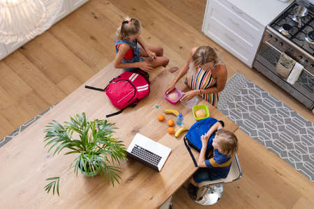 High angle view of caucasian mother with son and daughter preparing packed lunches in kitchen. happy family spending time together at home.の写真素材