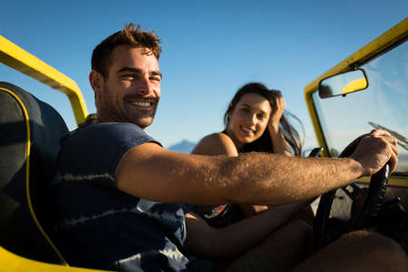 Happy caucasian couple sitting in beach buggy by the sea looking to camera. beach break on summer holiday road trip.の写真素材