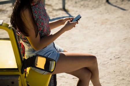 Midsection of caucasian woman sitting on beach buggy by the sea using smartphone. beach break on summer holiday road trip.の写真素材