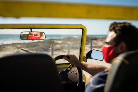 Caucasian man wearing face mask sitting in beach buggy reflected in mirror. beach stop off on summer...