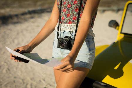 Midsection of caucasian woman leaning against beach buggy by the sea reading roadmap. beach break on summer holiday road trip.の写真素材