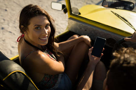 Happy caucasian couple sitting in beach buggy by the sea using smartphone. beach break on summer...