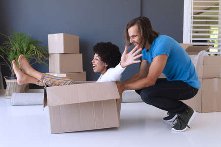 Happy diverse couple moving house smiling and playing with cartons. staying at home in isolation...
