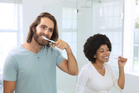 Diverse couple standing in bathroom brushing teeth. staying at home in isolation during quarantine...