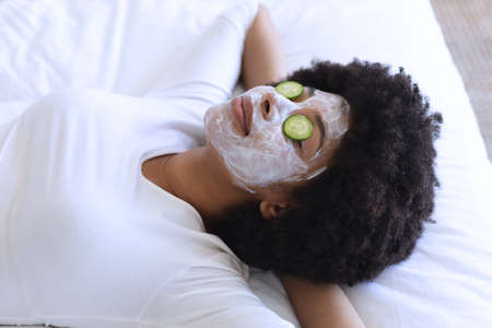 African american woman lying in bed wearing beauty mask. staying at home in isolation during quarantine lockdown.の写真素材