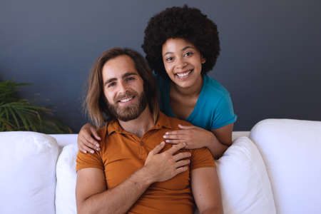 Portrait of happy diverse couple sitting on sofa embracing and smiling. staying at home in isolation...