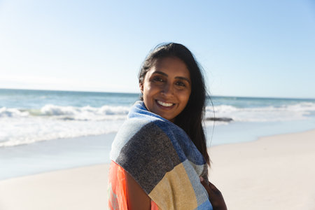 Portrait of smiling mixed race woman on beach holiday looking to camera. outdoor leisure vacation time by the sea.の写真素材