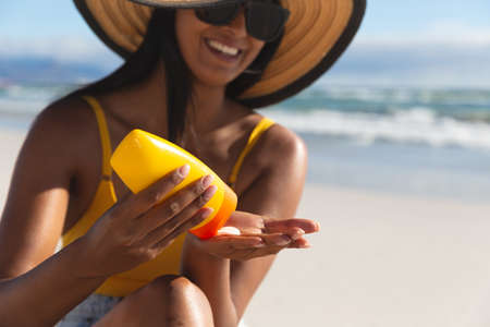 Smiling mixed race woman on beach holiday using sunscreen cream. vacation outdoor leisure time by...