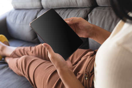 Mixed race gender fluid man relaxing at home on couch using tablet, with copy space screen. staying...