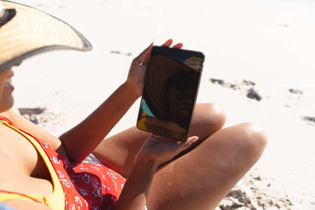 Mixed race woman on beach holiday using tablet. healthy outdoor leisure time by the sea.の写真素材