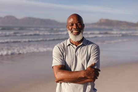 Portrait of senior african american man with arms crossed smiling while standing on the beach....
