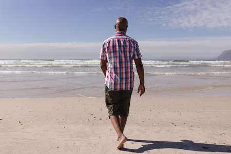 Rear view of senior african american man walking on the beach. travel vacation retirement lifestyle conceptの写真素材