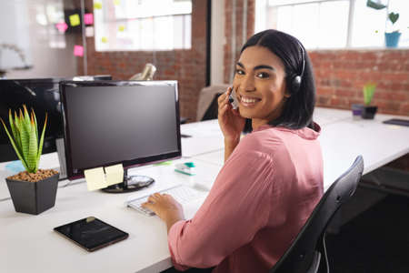 Happy mixed race businesswoman having video call sitting in front of computer using headphones....